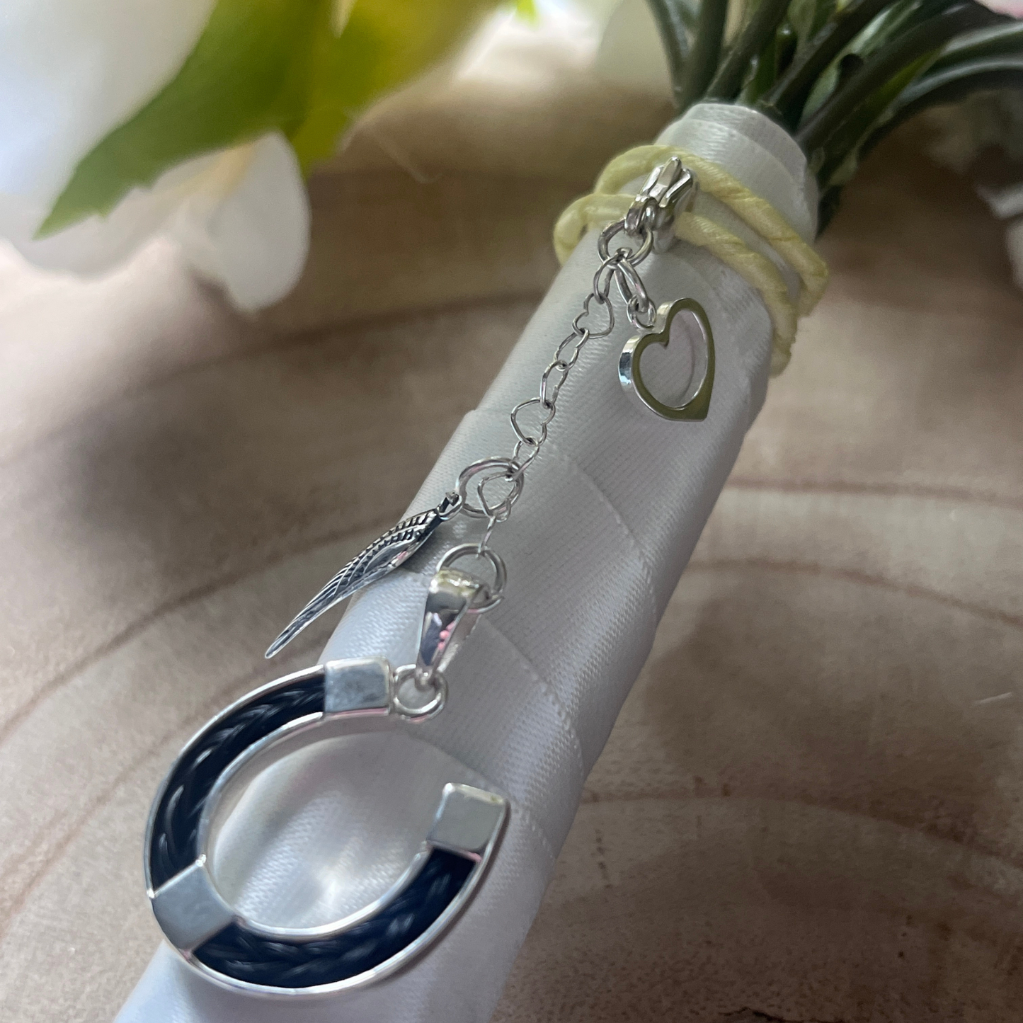Silver horsehair charm with heart and angel wing charms on a white ribbon against a neutral background