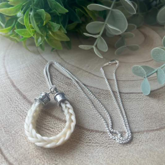 Necklace with a white braided pendant on a textured surface with green leaves in the background