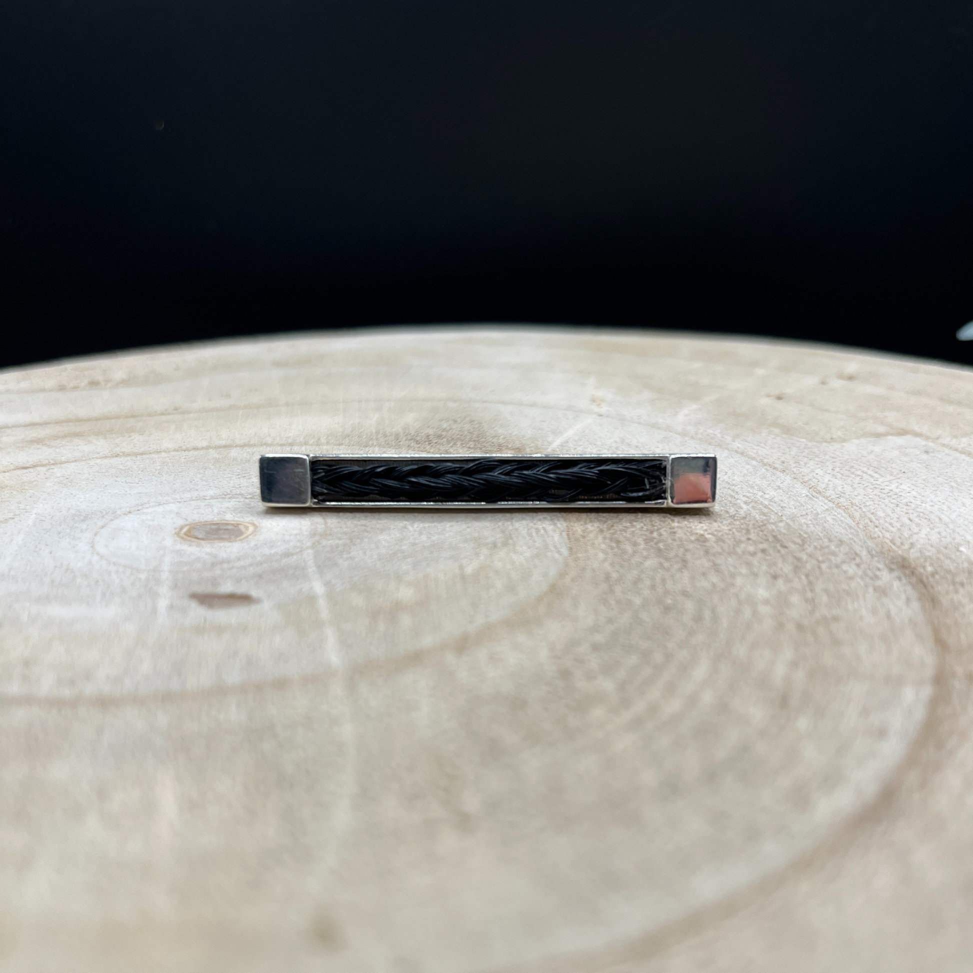 Silver stock pin with black braided design on a wooden surface