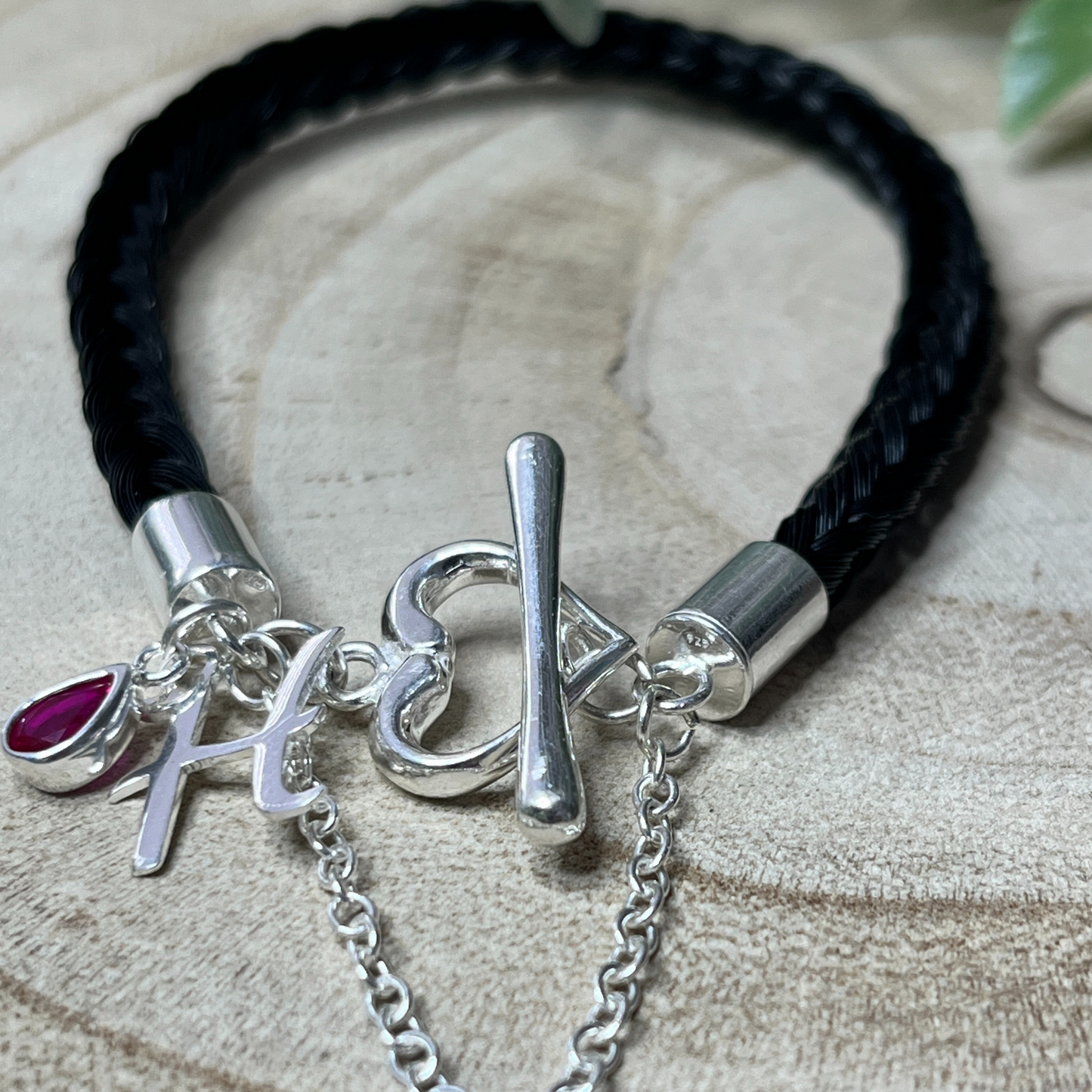 Bracelet with silver charms and a black braid on a textured surface