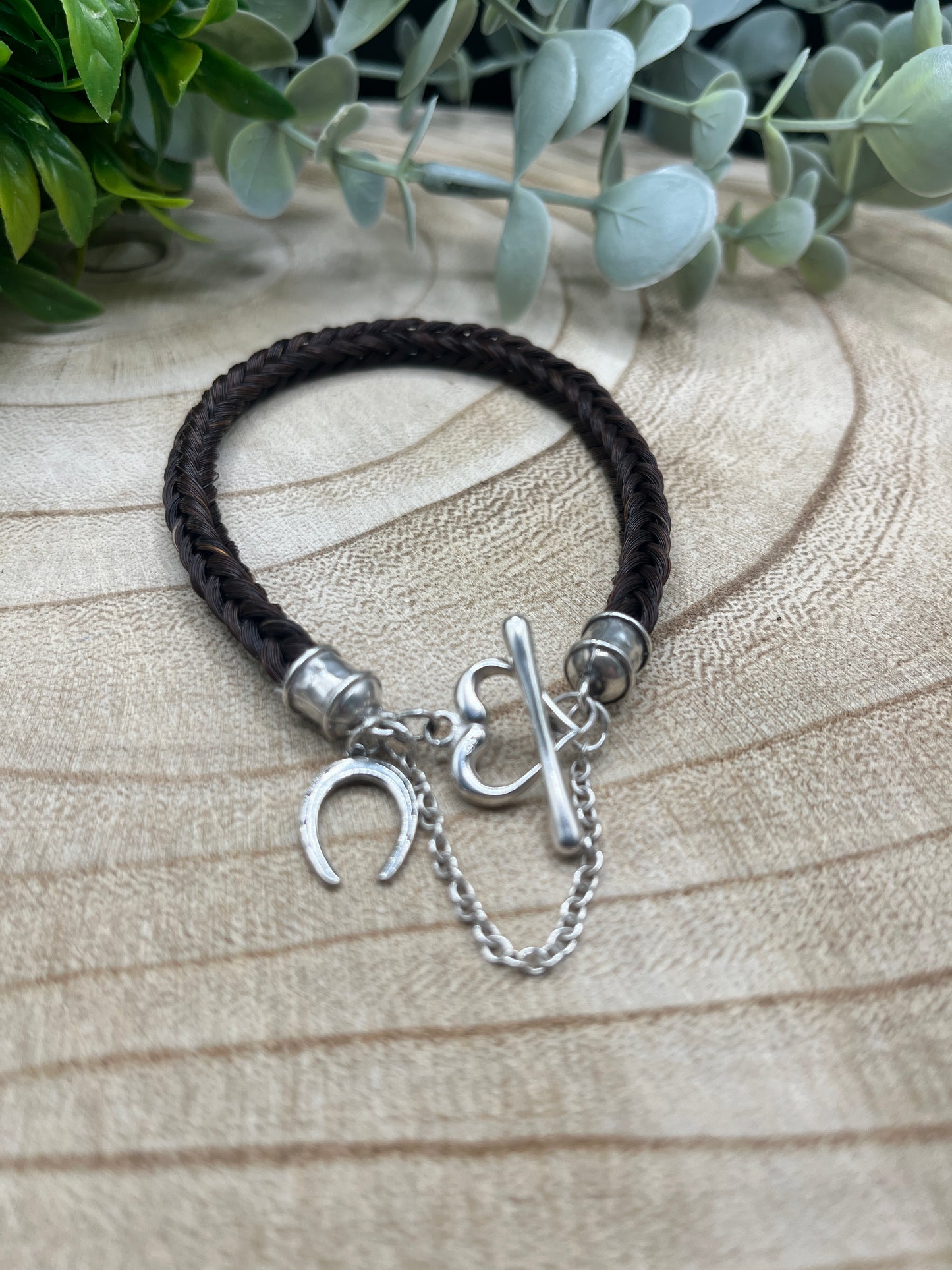 Black braided bracelet with silver charms on a textured surface