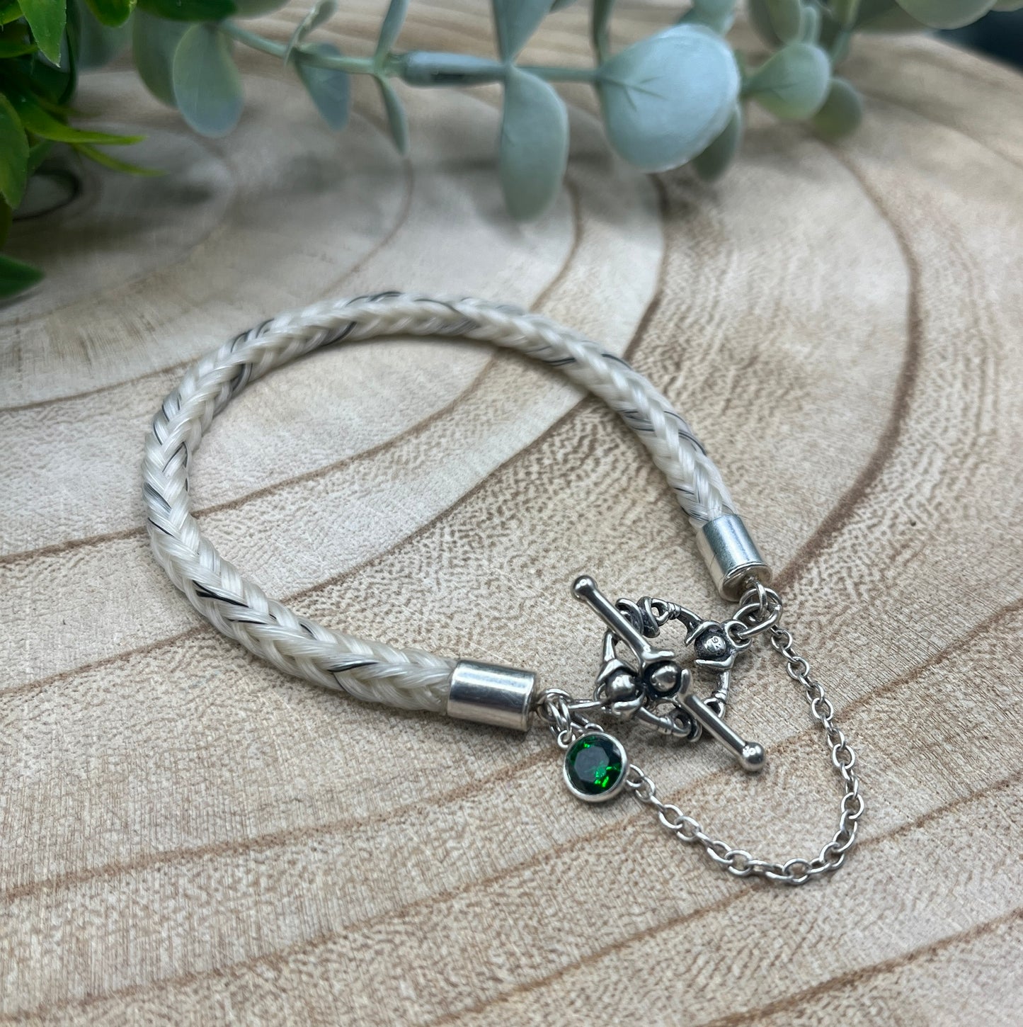 Silver bracelet with braided design and green gemstone on a wooden surface
