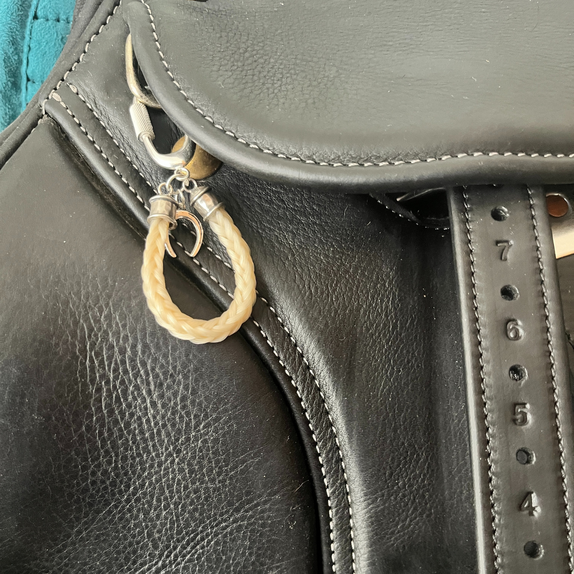 Close-up of a black leather saddle with a horse hair keychain hanging from it.