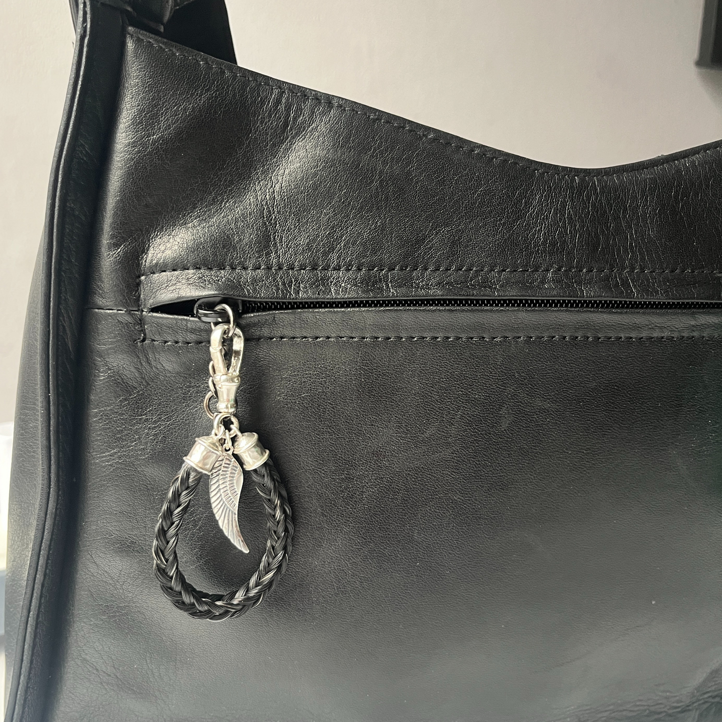 Black leather bag with a keychain featuring a braided design and feather detail.