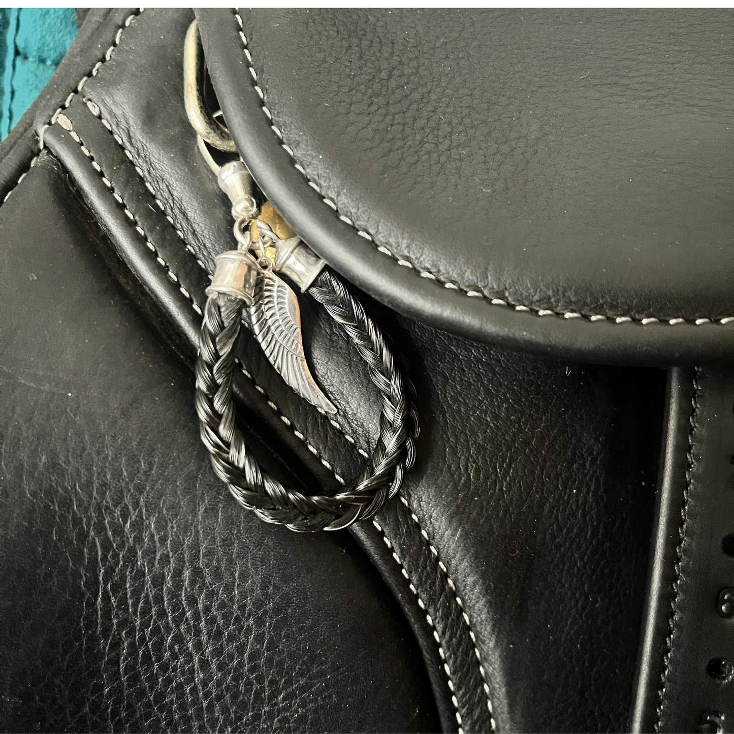 Black leather saddle with a braided keychain featuring a wing charm