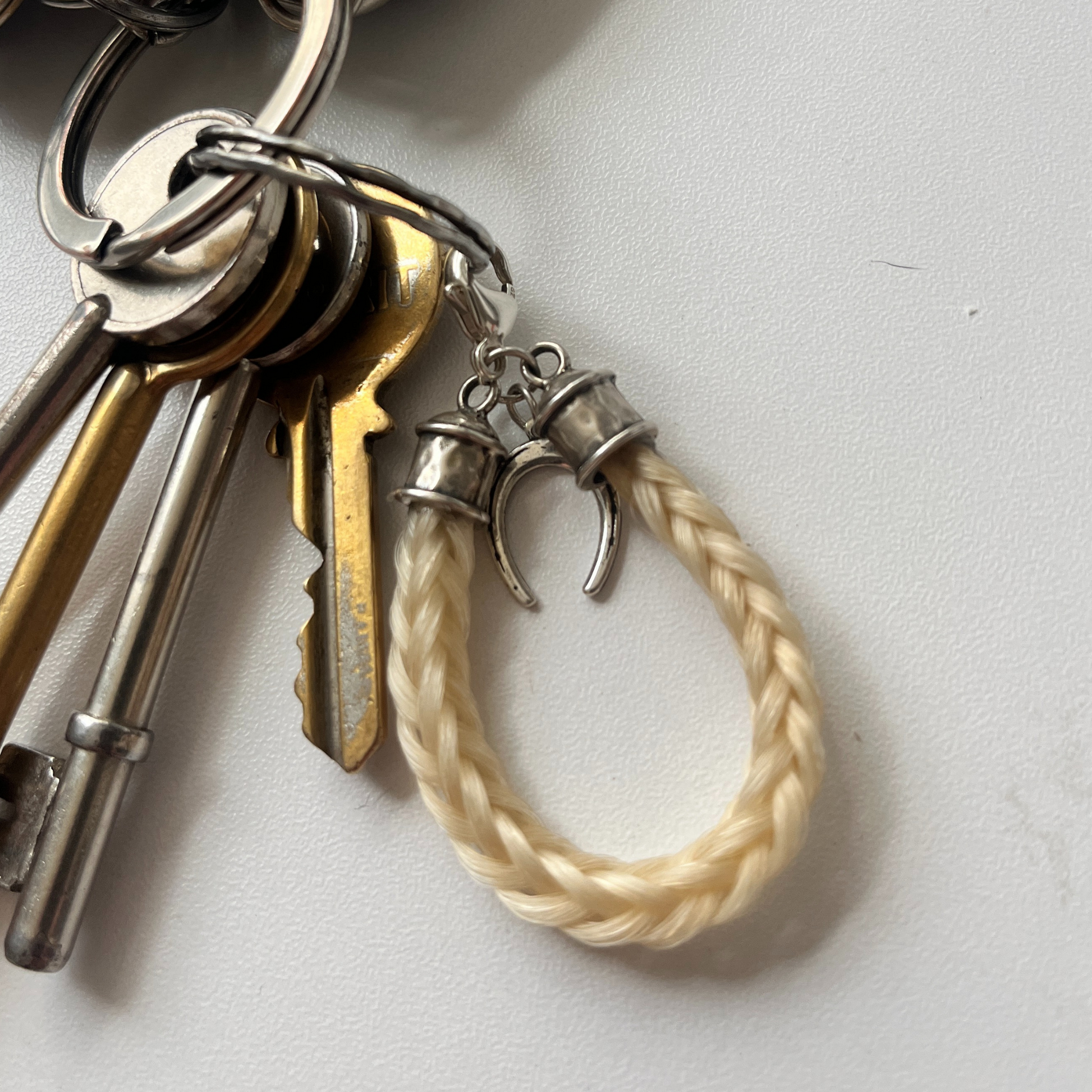 Keychain with keys and a braided white horsehair on a light grey background