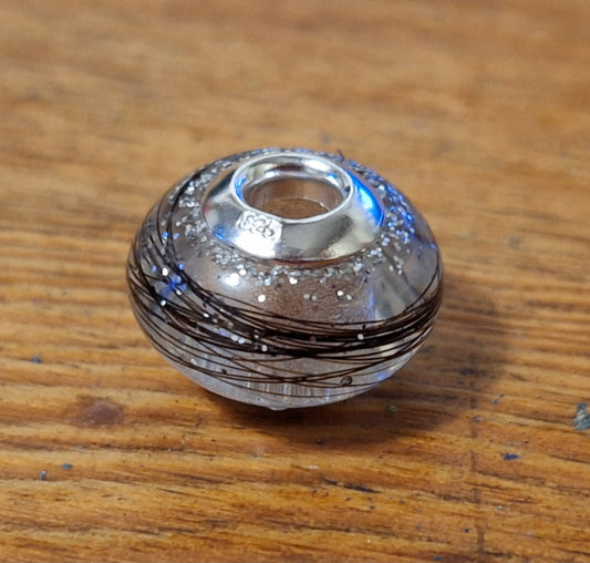 A clear resin bead with silver accents designed for use in hair or fur.