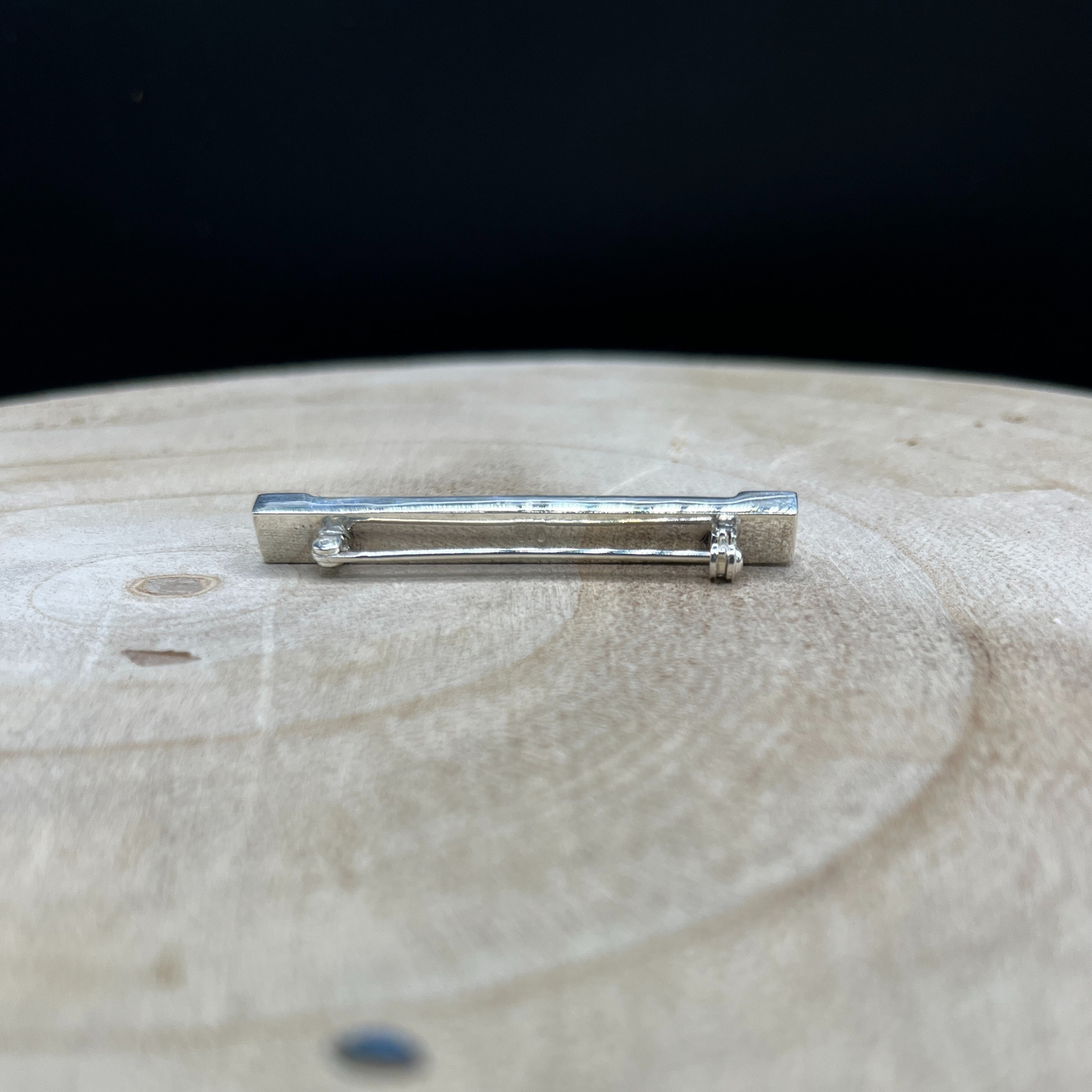 Silver bar brooch on a wooden surface with a black background
