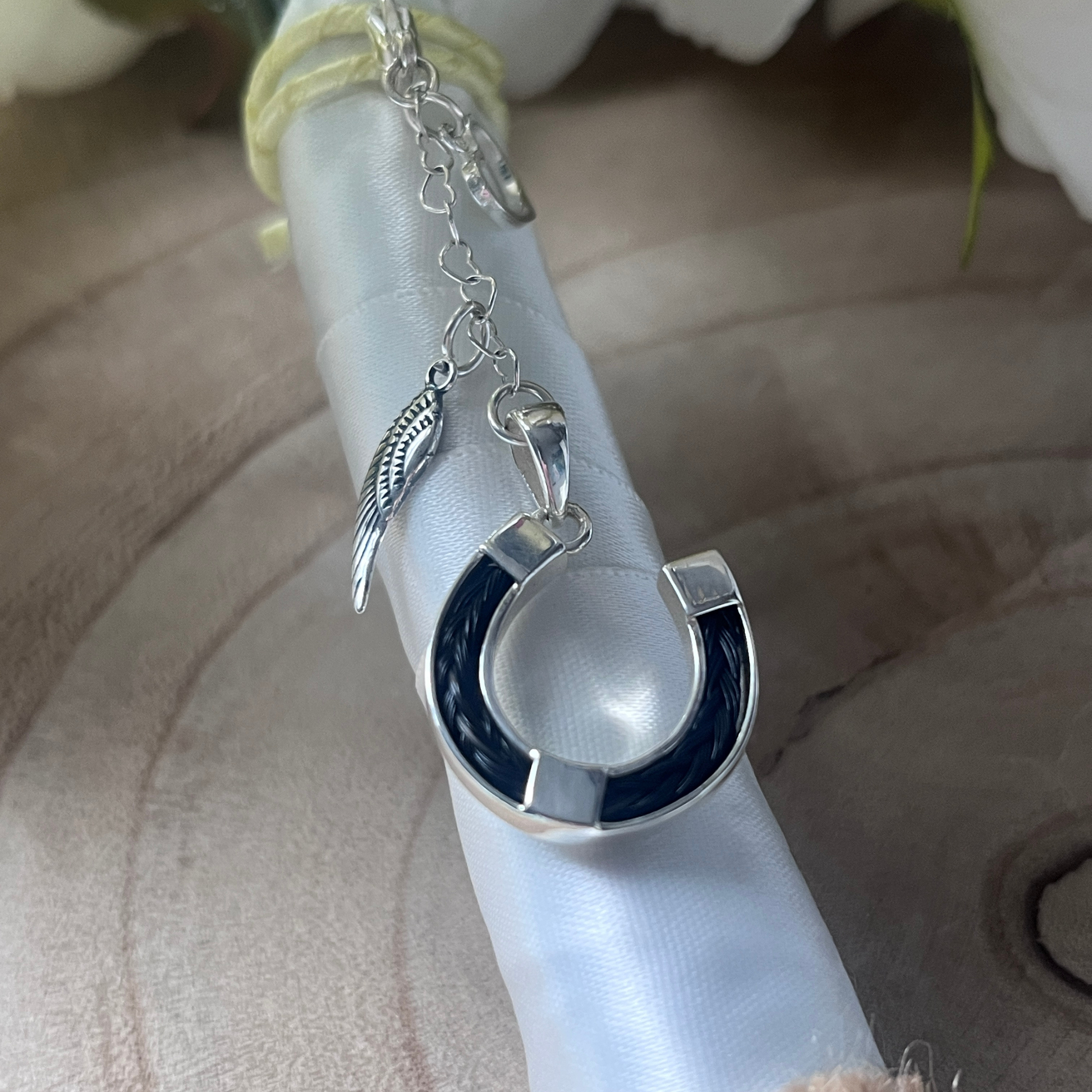 Silver horsehair charm with a blue accent on a white ribbon against a neutral background